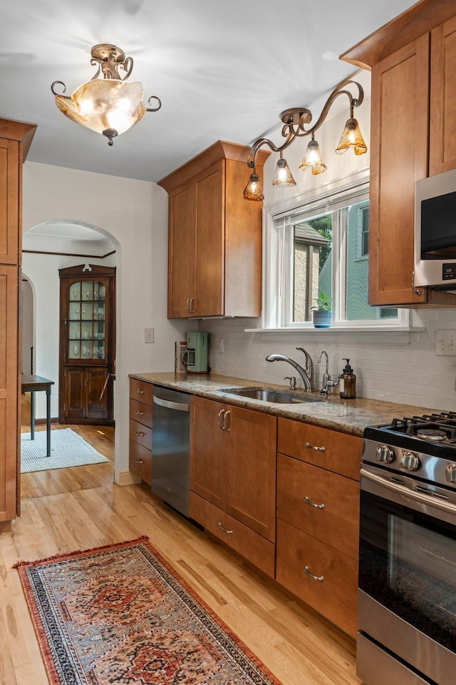 947 Stryker Ave W, Saint Paul, MN 55118 - kitchen with appliances with stainless steel finishes, arched walkways, light wood-style flooring, brown cabinetry, and tasteful backsplash