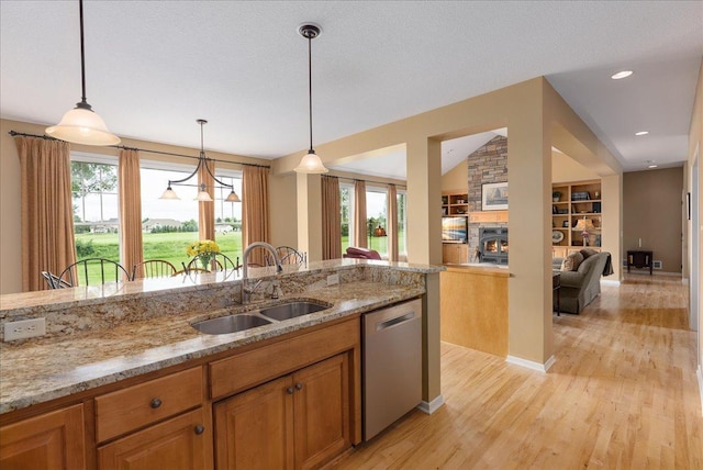 238 Muirfield Trl, Hudson, WI 54016 - kitchen with stainless steel dishwasher, light wood finished floors, light stone countertops, brown cabinetry, and decorative light fixtures