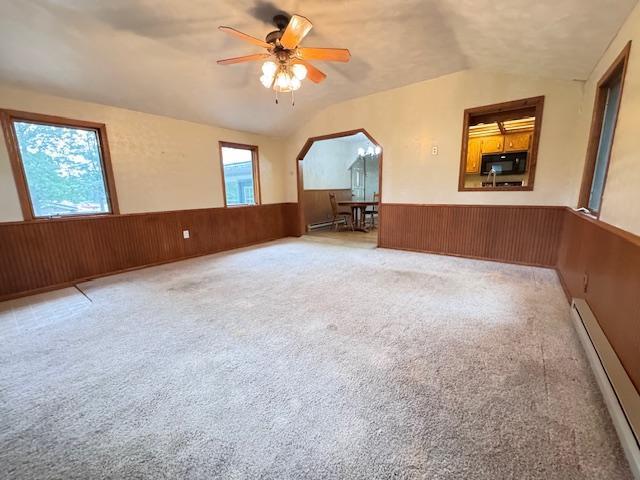 517 2nd St NW, Menahga, MN 56464 - unfurnished living room featuring a wainscoted wall, baseboard heating, lofted ceiling, wood walls, and ceiling fan