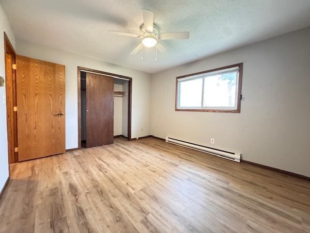 517 2nd St NW, Menahga, MN 56464 - unfurnished bedroom featuring a baseboard heating unit, light wood finished floors, a closet, a ceiling fan, and a textured ceiling