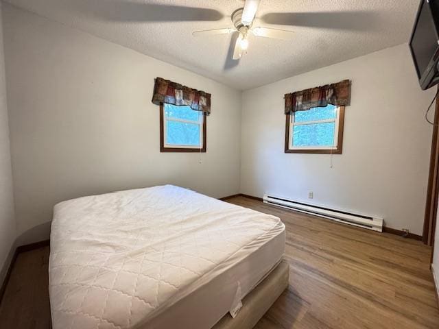 517 2nd St NW, Menahga, MN 56464 - bedroom with a baseboard heating unit, wood finished floors, ceiling fan, and a textured ceiling