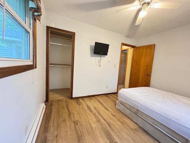 517 2nd St NW, Menahga, MN 56464 - bedroom with light wood-style flooring, baseboard heating, a closet, a textured ceiling, and a ceiling fan