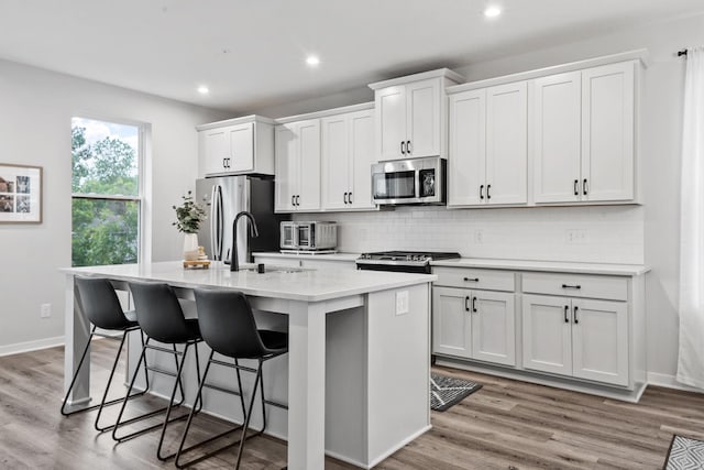 8612 Kenyon Ct NE Unit A, Blaine, MN 55449 - kitchen featuring stainless steel appliances, a kitchen island with sink, a breakfast bar area, light countertops, and tasteful backsplash