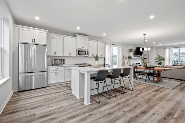 8612 Kenyon Ct NE Unit A, Blaine, MN 55449 - kitchen with appliances with stainless steel finishes, a kitchen island with sink, recessed lighting, light wood-style flooring, and light countertops