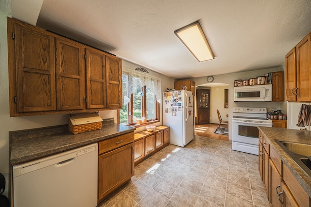 49227 US Highway 59, Dunn Twp, MN 56587 - kitchen featuring white appliances, arched walkways, dark countertops, and brown cabinetry
