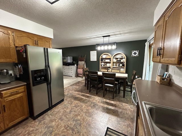 605 Park Island Dr SW, Hutchinson, MN 55350 - kitchen featuring stainless steel fridge with ice dispenser, dark countertops, brown cabinets, a textured ceiling, and decorative light fixtures