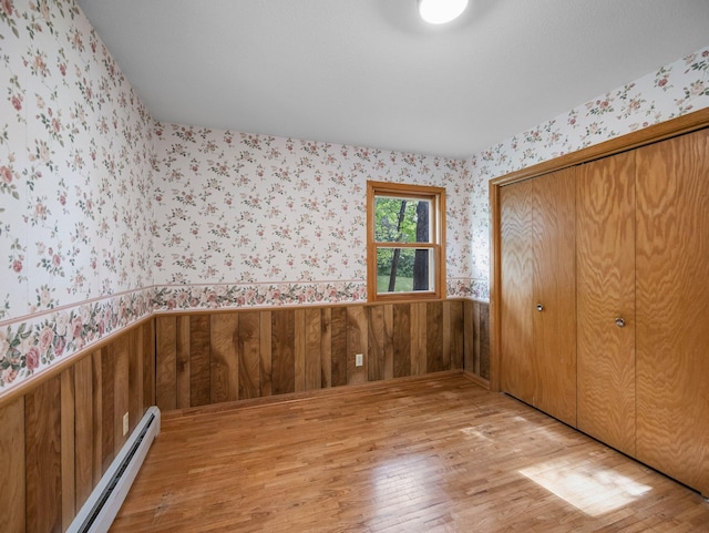8545 70th St NW, Annandale, MN 55302 - unfurnished bedroom with a baseboard heating unit, wallpapered walls, light wood-style floors, wainscoting, and a closet