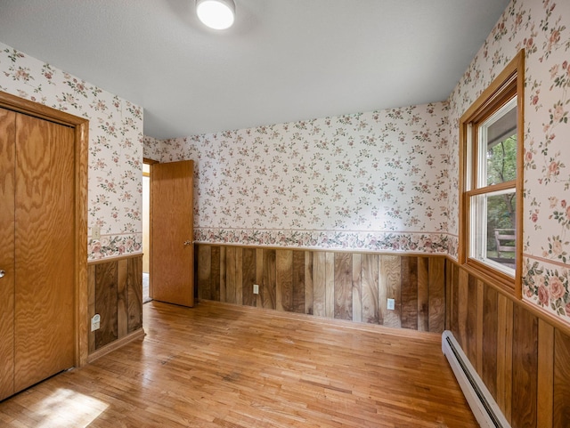 8545 70th St NW, Annandale, MN 55302 - unfurnished room with a baseboard radiator, wood finished floors, wallpapered walls, a wainscoted wall, and wood walls