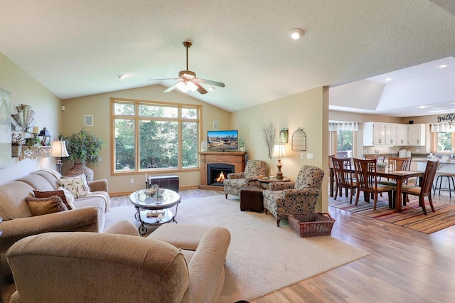 2301 170th Ln NW, Andover, MN 55304 - living area featuring lofted ceiling, light wood-style flooring, ceiling fan, a warm lit fireplace, and a textured ceiling