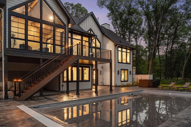 4864 148th Ave, Ham Lake, MN 55304 - back of house at dusk with a hot tub, stairway, a patio, an outdoor pool, and board and batten siding