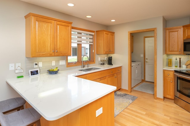 5209 Goodview Ln NW, Rochester, MN 55901 - kitchen featuring stainless steel appliances, washing machine and clothes dryer, a peninsula, light wood-style flooring, and tasteful backsplash