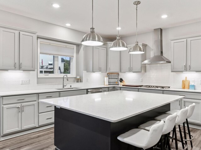 7154 Alphabet St, Chanhassen, MN 55317 - kitchen with wall chimney range hood, a kitchen island, light wood-type flooring, stainless steel gas stovetop, and backsplash