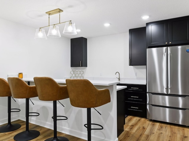 7154 Alphabet St, Chanhassen, MN 55317 - kitchen featuring freestanding refrigerator, a kitchen breakfast bar, dark cabinets, light wood-type flooring, and light countertops