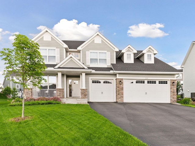 7154 Alphabet St, Chanhassen, MN 55317 - view of front facade with asphalt driveway, stone siding, a front lawn, covered porch, and roof with shingles