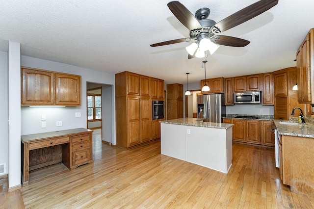 2319 Viola View Ln NE, Rochester, MN 55906 - kitchen with stainless steel appliances, light wood-type flooring, brown cabinetry, a kitchen island, and light stone countertops
