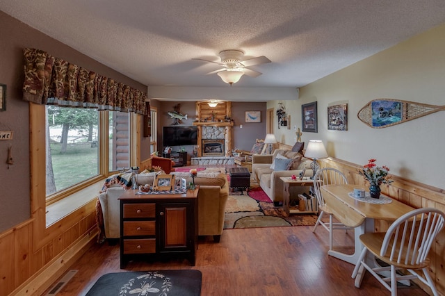 35139 County 39, Laporte, MN 56461 - living room featuring a textured ceiling, dark wood-style floors, wainscoting, a ceiling fan, and a fireplace