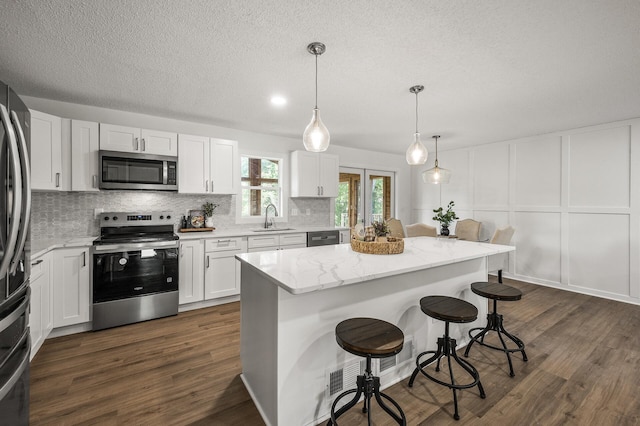 4909 98th St, Bloomington, MN 55437 - kitchen with appliances with stainless steel finishes, backsplash, a breakfast bar area, dark wood-style flooring, and white cabinetry