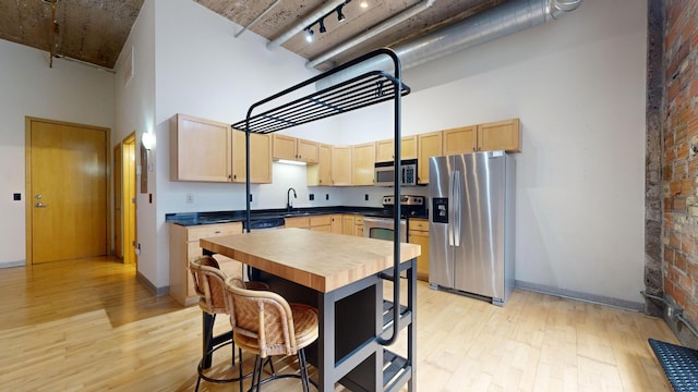521 7th St Unit 519, Minneapolis, MN 55415 - kitchen with stainless steel appliances, a towering ceiling, light brown cabinetry, light wood finished floors, and butcher block counters