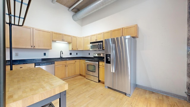 521 7th St Unit 519, Minneapolis, MN 55415 - kitchen featuring stainless steel appliances, light brown cabinets, a high ceiling, light wood-style floors, and dark countertops