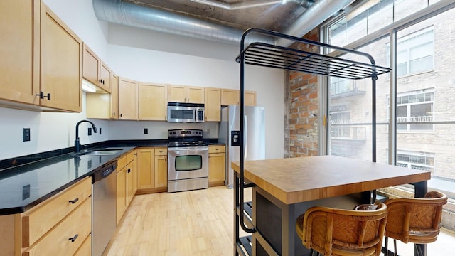 521 7th St Unit 519, Minneapolis, MN 55415 - kitchen featuring appliances with stainless steel finishes, light brown cabinetry, light wood-style floors, dark countertops, and a towering ceiling