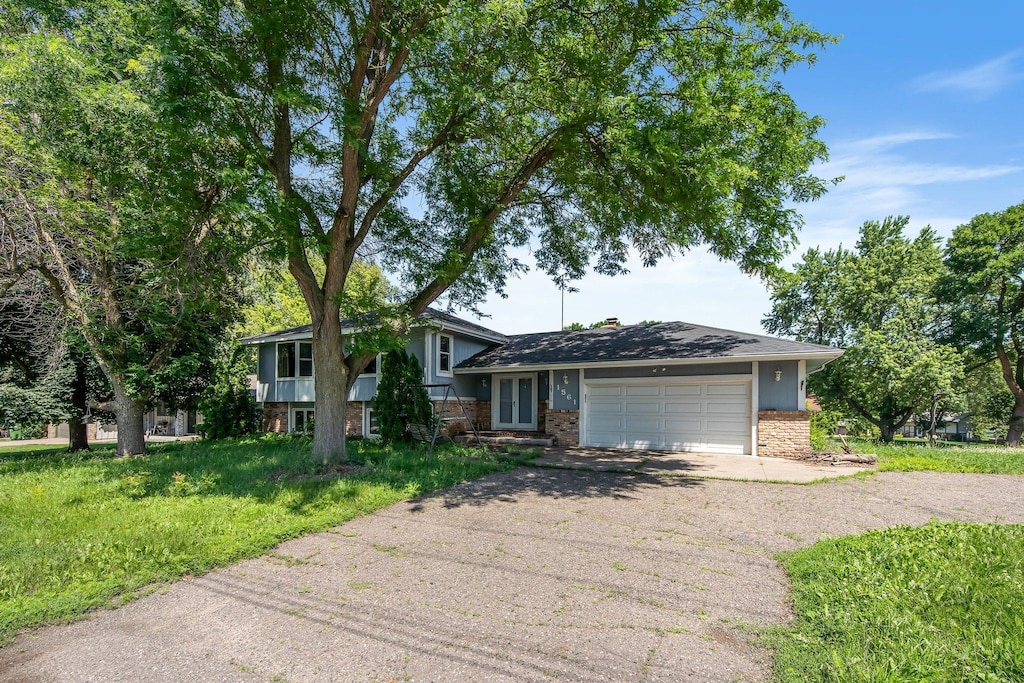 1561 Rice Creek Rd NE, Fridley, MN 55432 - split level home featuring driveway, an attached garage, brick siding, and a chimney