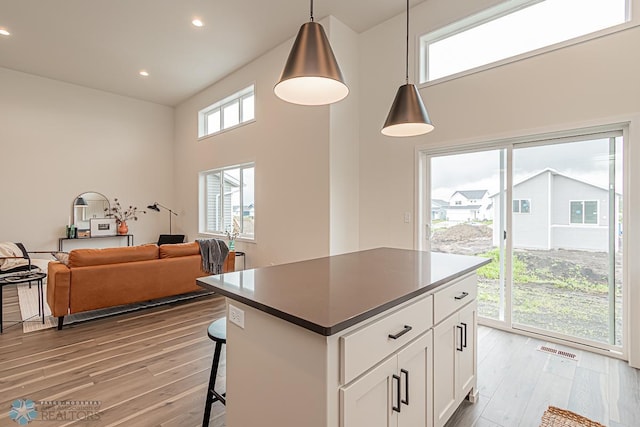 6724 32nd St S, Fargo, ND 58104 - kitchen with light wood-style flooring, white cabinetry, a breakfast bar area, a towering ceiling, and decorative light fixtures