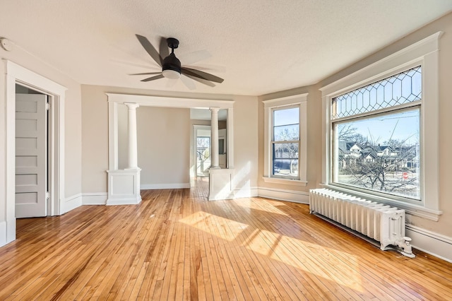 3148 Pleasant Ave, Minneapolis, MN 55408 - empty room with radiator heating unit, decorative columns, light wood-type flooring, a ceiling fan, and a textured ceiling