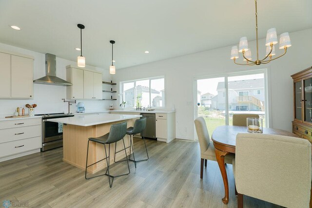 7328 Aquiline Dr S, Fargo, ND 58104 - kitchen with wall chimney exhaust hood, stainless steel appliances, light countertops, light wood-style floors, and a kitchen breakfast bar