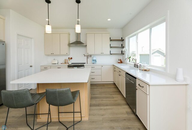 7328 Aquiline Dr S, Fargo, ND 58104 - kitchen with wall chimney range hood, appliances with stainless steel finishes, light wood-style floors, a kitchen bar, and a center island