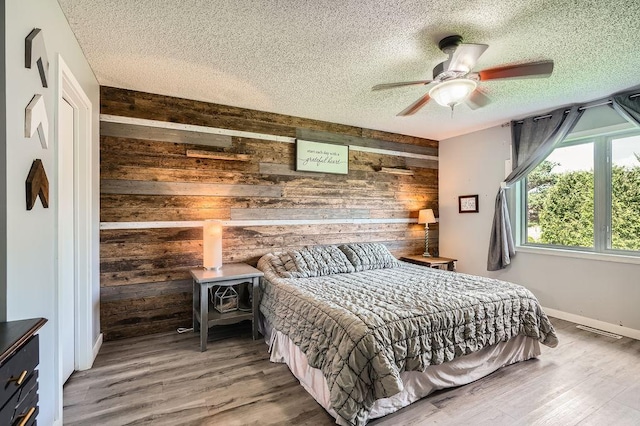 1301 English Ave NW, New Prague, MN 56071 - bedroom with wood walls, a textured ceiling, a wood stove, wood finished floors, and ceiling fan