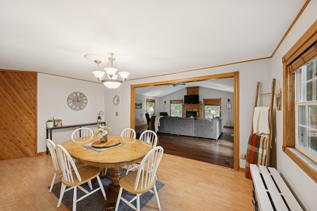 9372 71st St NE, Spicer, MN 56288 - dining area with light wood-type flooring, a warm lit fireplace, wooden walls, a chandelier, and vaulted ceiling