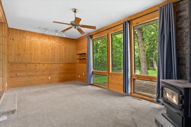 2224 75th Ave Unit M, Osceola, WI 54020 - unfurnished room featuring a wood stove, wood walls, track lighting, ceiling fan, and carpet