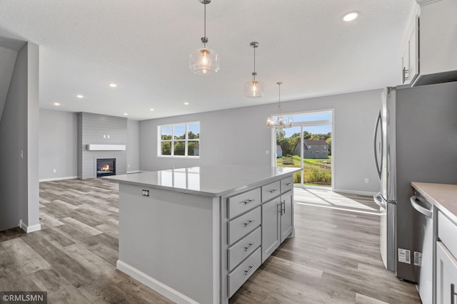 17205 61st St NE, Otsego, MN 55330 - kitchen featuring a large fireplace, a kitchen island, light countertops, stainless steel appliances, and light wood-style floors