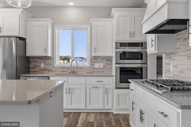 17205 61st St NE, Otsego, MN 55330 - kitchen with custom range hood, stainless steel appliances, backsplash, white cabinetry, and wood finished floors