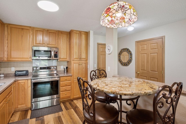 1600 Arundel St Unit 201, Saint Paul, MN 55117 - kitchen with stainless steel appliances, light wood-style floors, backsplash, light stone countertops, and decorative light fixtures