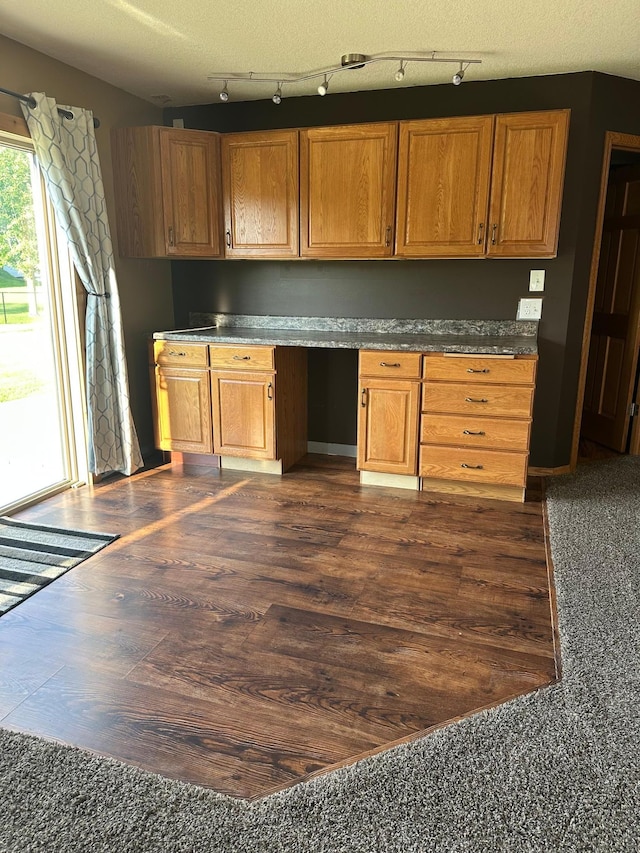2460 Fox Hollow Ln, Owatonna, MN 55060 - kitchen featuring rail lighting, built in desk, dark wood finished floors, and dark countertops