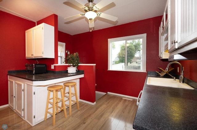 1341 3rd Ave N, Fargo, ND 58102 - kitchen featuring light wood-type flooring, white cabinetry, dark countertops, a kitchen bar, and ceiling fan