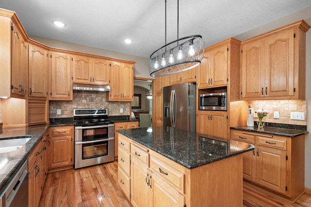 842 Vista Cir, Delano, MN 55328 - kitchen featuring appliances with stainless steel finishes, under cabinet range hood, light wood-style flooring, decorative backsplash, and arched walkways