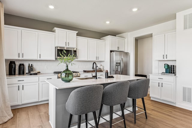 7588 Norway Ln, Lino Lakes, MN 55038 - kitchen with appliances with stainless steel finishes, a center island with sink, a breakfast bar area, decorative backsplash, and light wood-style flooring