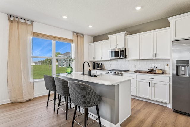 7588 Norway Ln, Lino Lakes, MN 55038 - kitchen featuring appliances with stainless steel finishes, light wood-type flooring, a kitchen island with sink, a breakfast bar area, and recessed lighting