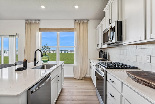 7588 Norway Ln, Lino Lakes, MN 55038 - kitchen with stainless steel appliances, light wood-style floors, backsplash, a kitchen island with sink, and white cabinets
