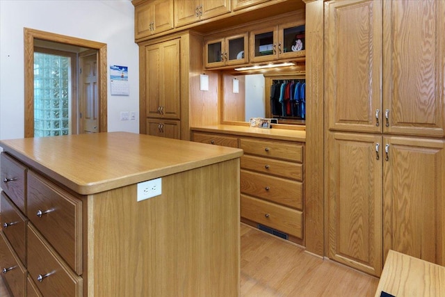 2719 Spring Lake Rd SW, Prior Lake, MN 55372 - kitchen featuring light wood-type flooring, a kitchen island, glass insert cabinets, light countertops, and brown cabinets