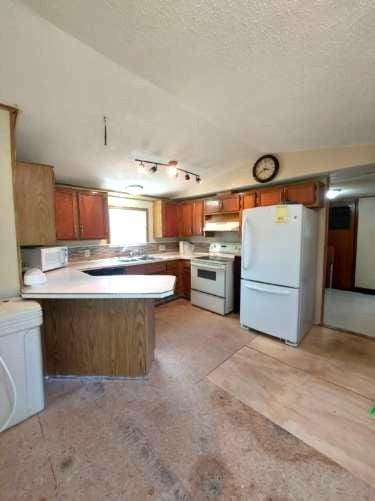 1329 US Highway 8, Balsam Lake, WI 54001 - kitchen with white appliances, brown cabinets, a peninsula, lofted ceiling, and under cabinet range hood