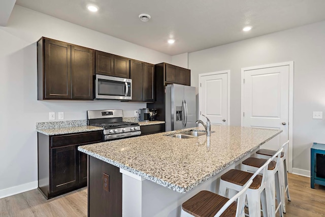 11242 131st Cir N, Dayton, MN 55327 - kitchen featuring appliances with stainless steel finishes, light wood-style flooring, a breakfast bar, an island with sink, and dark brown cabinets