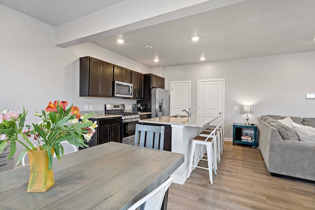 11242 131st Cir N, Dayton, MN 55327 - kitchen with stainless steel appliances, open floor plan, dark brown cabinets, light wood-style flooring, and a kitchen island with sink
