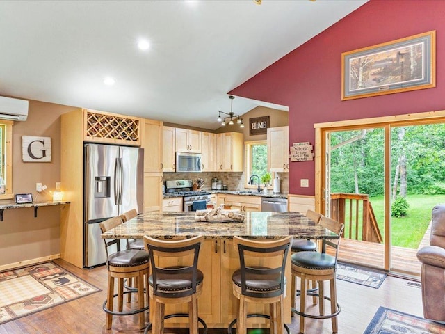 31591 Summer Dr, Breezy Point, MN 56472 - kitchen featuring appliances with stainless steel finishes, vaulted ceiling, a wall unit AC, light stone counters, and a kitchen breakfast bar