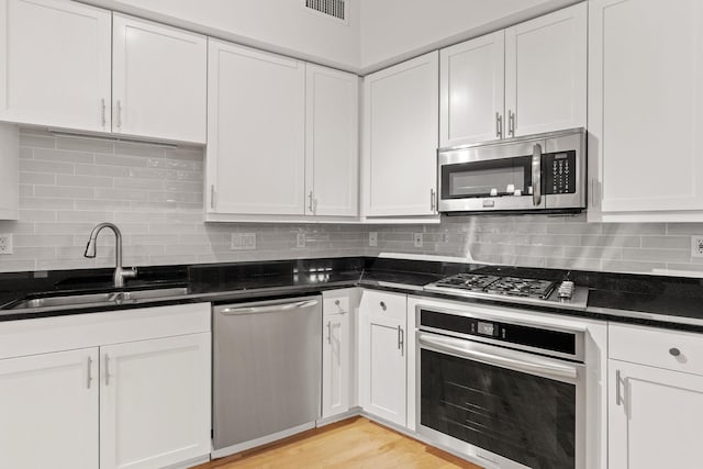 408 1st St Unit 310, Minneapolis, MN 55401 - kitchen with appliances with stainless steel finishes, white cabinets, backsplash, light wood-type flooring, and dark stone counters
