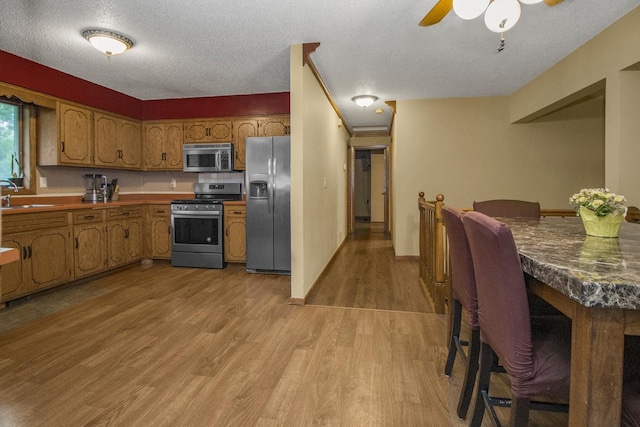 2246 Vivian Ln, Saint Paul, MN 55119 - kitchen with stainless steel appliances, brown cabinetry, light wood-type flooring, a ceiling fan, and a textured ceiling