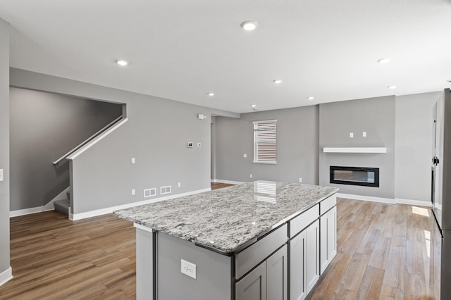 11263 131st Cir N, Dayton, MN 55327 - kitchen with light wood-style floors, a glass covered fireplace, light stone countertops, a kitchen island, and recessed lighting