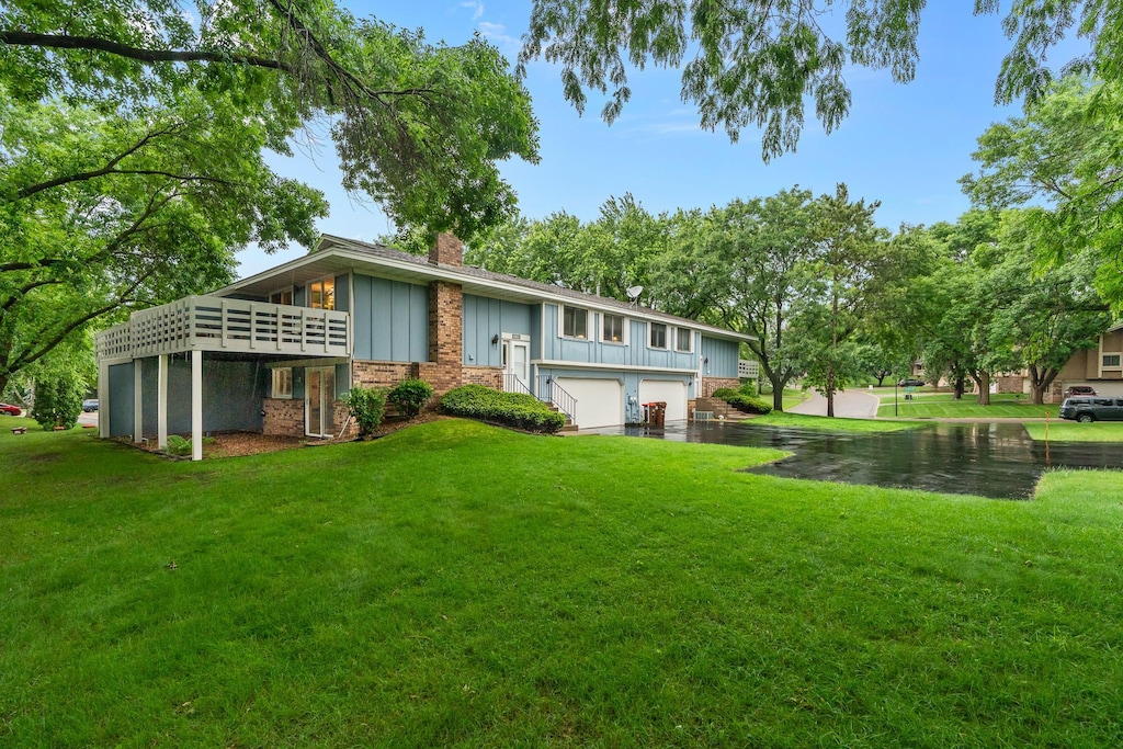 6881 Stratford Rd, Woodbury, MN 55125 - back of house featuring board and batten siding, a garage, a chimney, a lawn, and a deck